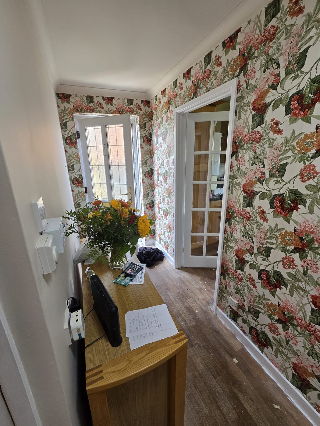 Hallway hung with a large floral wallpaper, with white woodwork and glazed doors