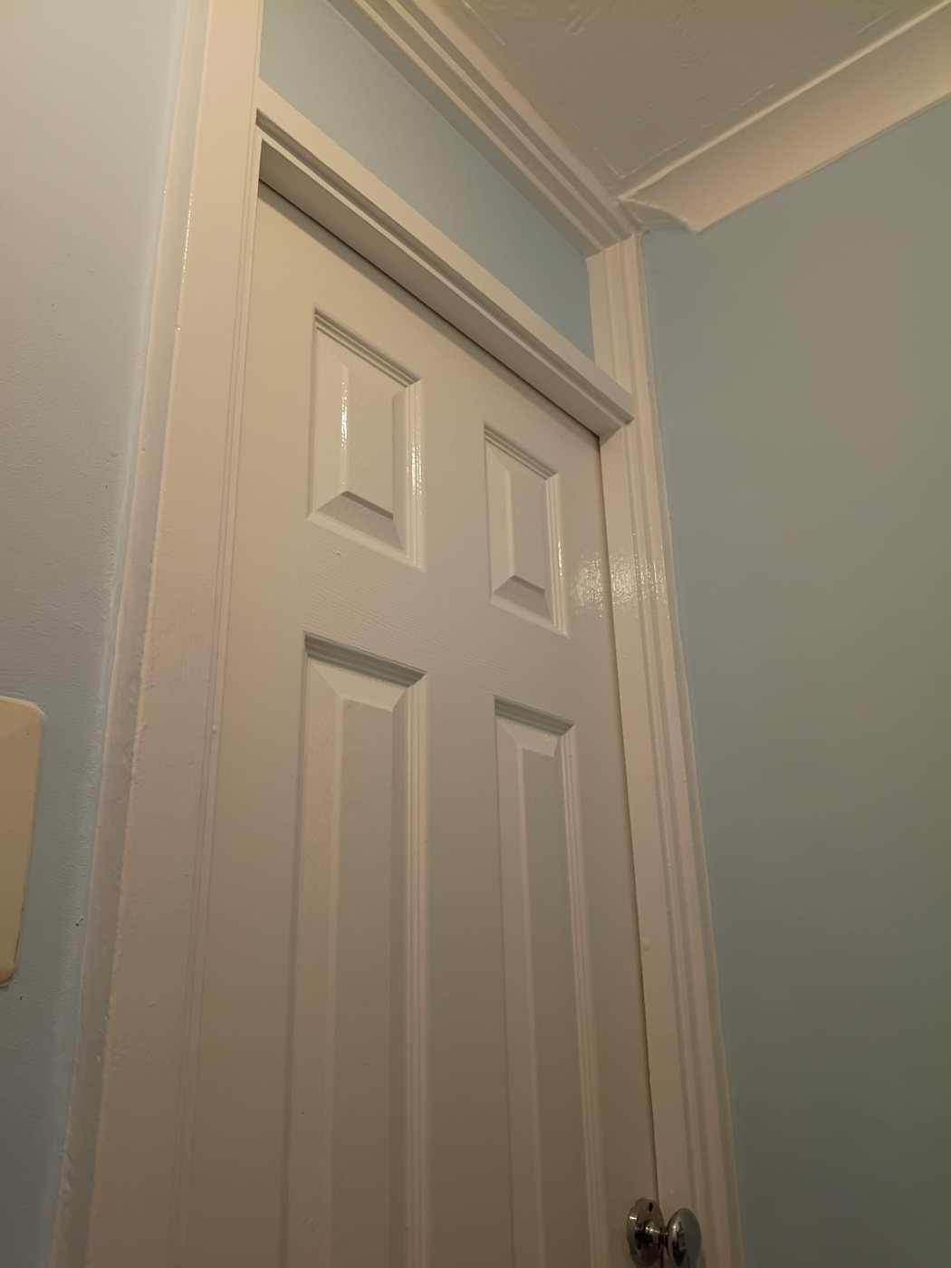 Glossed white panelled door, frame and cornice against pale blue walls, Little Common