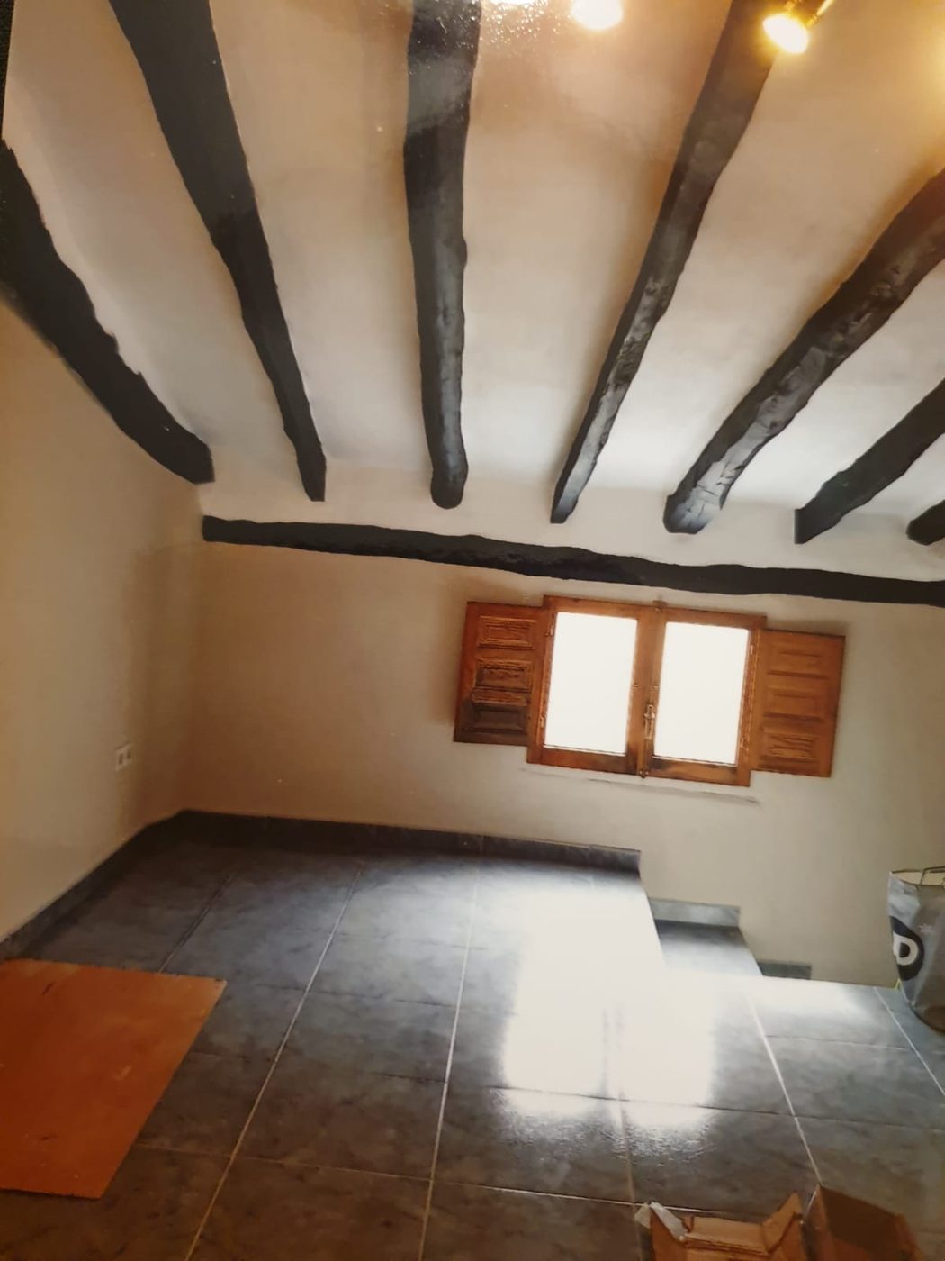 Room with dark painted ceiling beams over a freshly painted white ceiling and walls