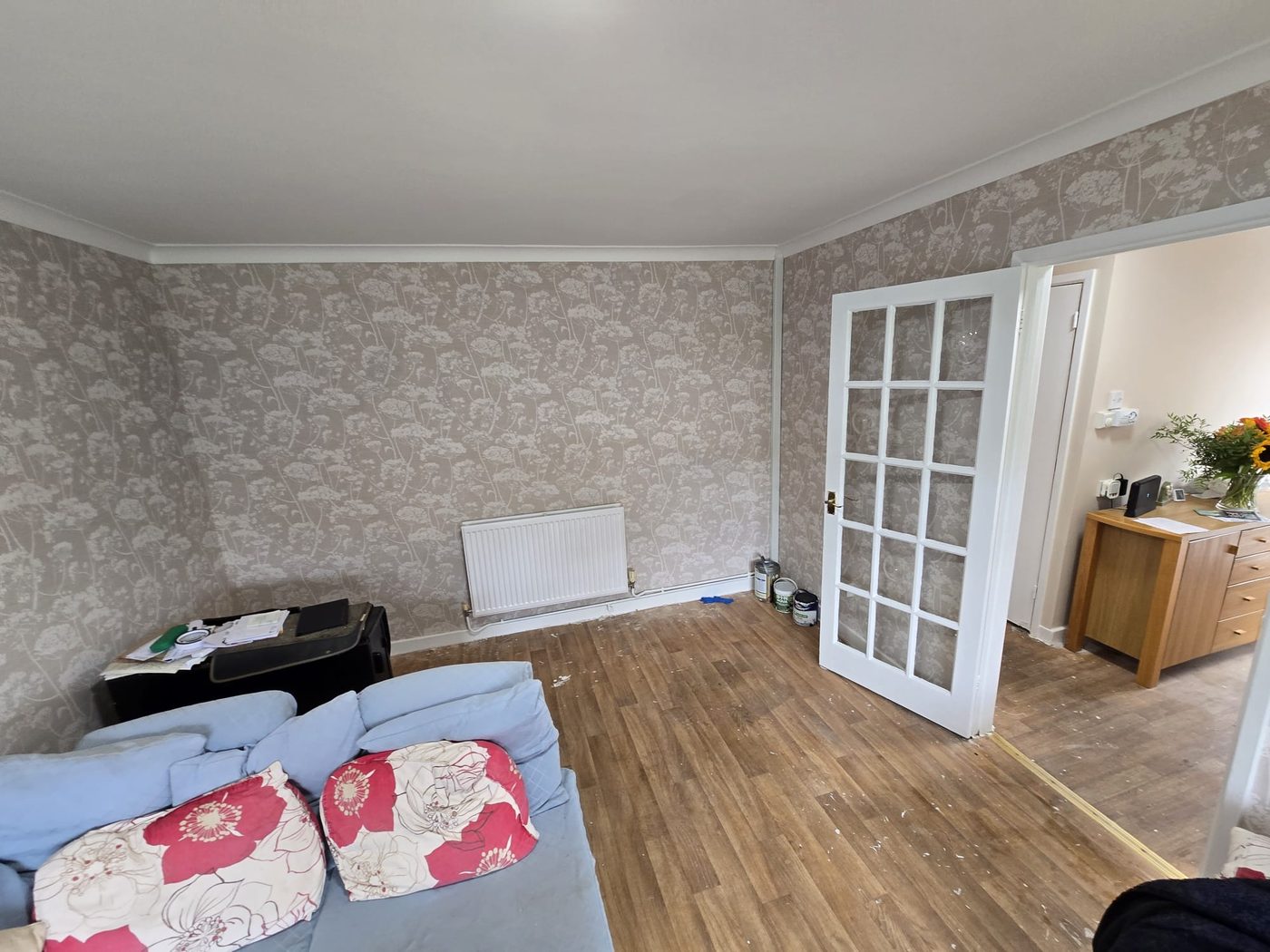 Living room papered in a grey and white patterned wallpaper, with white coving and a glazed door